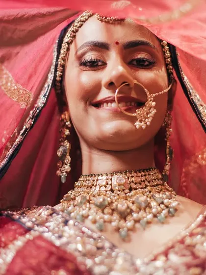 A joyful smile from the bride, Bhavita, from under her veil. This close-up captures her happiness and the intricate details of her bridal look.