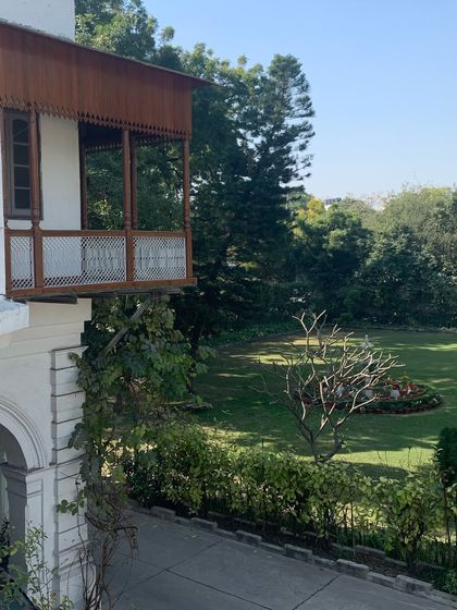 A restored timber balcony on a Delhi bungalow, providing a beautiful transition space between the interior and the lush garden.