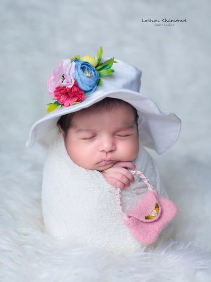 A very chic and stylish pose with a baby in a white wrap, wearing a fashionable hat and holding a tiny pink purse.