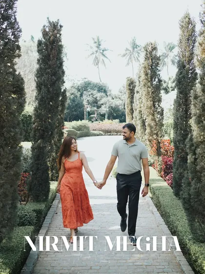 The couple walks hand-in-hand down a path lined with tall cypress trees, creating a beautiful, symmetrical, and romantic pre-wedding photograph.
