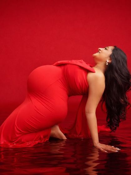 This powerful image captures a moment of pure joy. The mom-to-be, in a striking red gown, leans back into a digitally created water effect, resulting in a unique and artistic maternity photo.