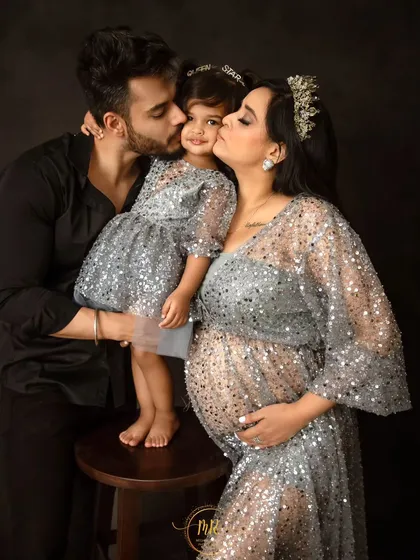 A beautiful family portrait with matching outfits. The partner and mother-to-be kiss their daughter's cheeks, all dressed in sparkling silver for a glamorous look.