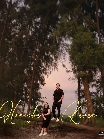 A dramatic portrait of the couple in a forest near the beach at dusk. The unique framing and handwritten-style names add a personalized, artistic touch to their pre-wedding photo.