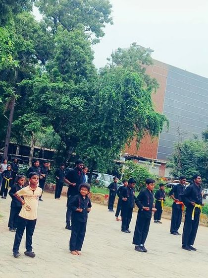 A wide shot of an outdoor class with students of all ages lined up. You can see young children and adults training side by side, all focused on their practice.