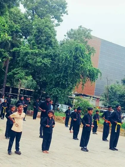 A wide shot of an outdoor class with students of all ages lined up. You can see young children and adults training side by side, all focused on their practice.