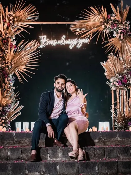 The happy couple posing in front of the 'It was always you' neon sign, a perfect centerpiece for their romantic proposal decor.