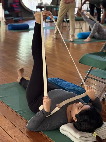 The Iyengar yoga belt is more than a prop. It is a teacher. It helps deepen stretches, supports restorative practices, and aids those with physical limitations. Here, it is used to extend the leg while keeping the shoulders and back relaxed on the floor.