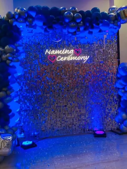 The same naming ceremony setup under deep blue lighting. This shows how versatile a sequin wall can be for creating different moods throughout an event.