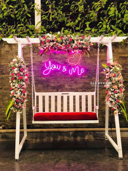 A full view of the elegant floral swing with its "You & Me" neon sign. This has become one of our most requested photo booth setups, blending modern romance with beautiful floral design.