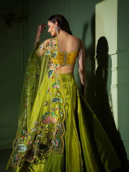 A view of the back of the lime green embroidered lehenga, highlighting the deep-back blouse design and the continuation of the floral artwork.