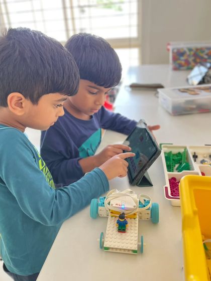 Our summer camps are designed to be interactive and engaging. Here, two students use a tablet to program their LEGO robot, learning the basics of coding and seeing their commands execute in real-time.