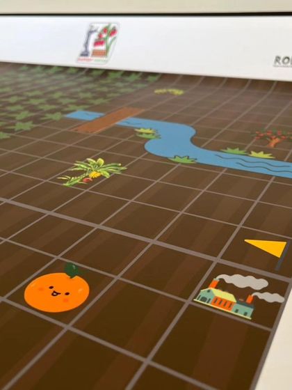 This section of the Explorers mat shows various illustrated elements like a river and an orange, creating a fun and engaging story for the young coders to follow.