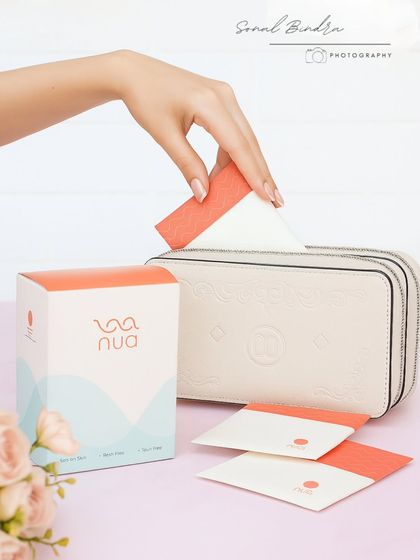 This lifestyle shot shows a hand placing a sanitary pad into a purse, highlighting its convenience and discreet design. The clean, minimal styling communicates a message of stress-free period care.