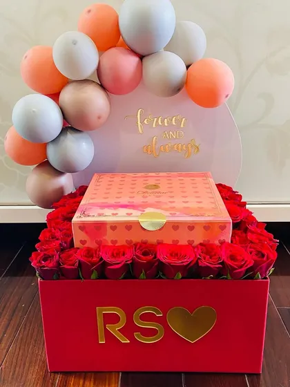 An incredibly romantic gesture. This custom red box is filled with a bed of perfect red roses, a gift box, and a personalized balloon arch that says 'Forever & always'.