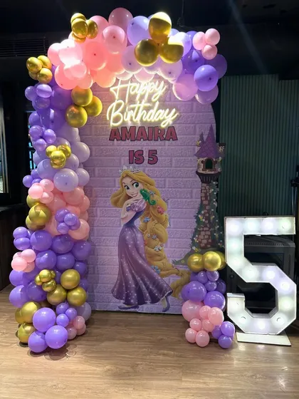 A lovely Princess Rapunzel theme for a 5th birthday, with a purple and pink balloon arch framing a themed backdrop and marquee number.