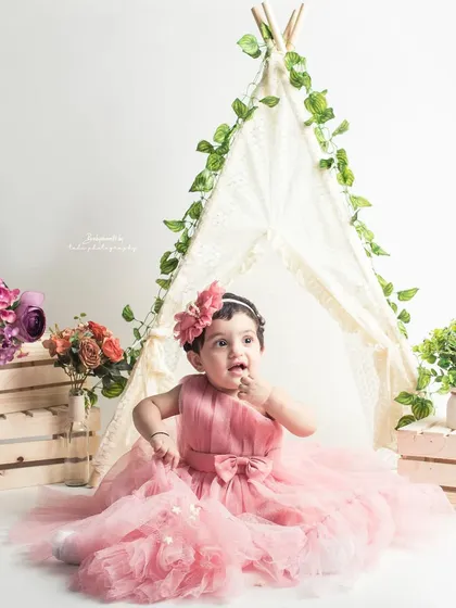 A beautiful princess in a fluffy pink dress, surrounded by flowers and a teepee for her first birthday portrait.