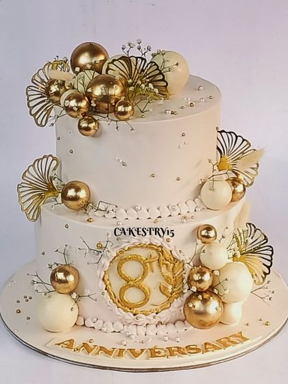 An elegant two-tier anniversary chocolate cake. This 3kg fawn-colored cake is adorned with shimmering gold balls, baby's breath, and an "8th Anniversary" plaque.