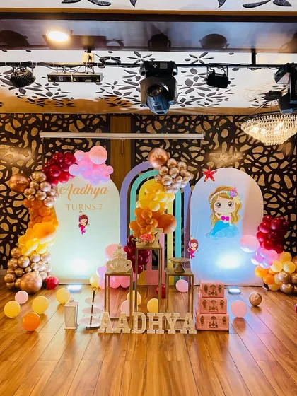 A royal birthday celebration with a princess theme. This setup features multiple arched backdrops, character cutouts, and a beautiful balloon arrangement in rose gold, pink, and orange tones.