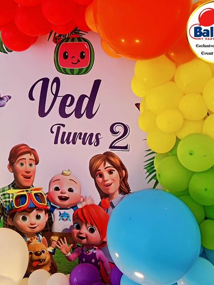 A close-up of a Cocomelon-themed backdrop, featuring the whole family and a colorful rainbow balloon garland.
