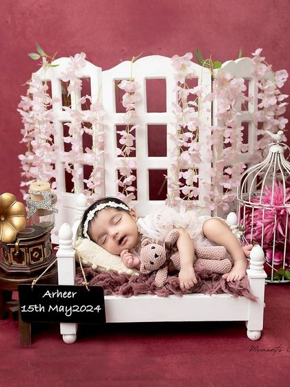 A princess in her floral chamber. This elegant setup features a newborn sleeping on a miniature bed, surrounded by hanging pink flowers and vintage props.