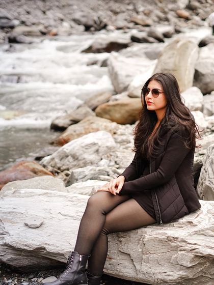 A beautiful solo shot of the bride-to-be sitting by a rocky stream in Manali, looking chic and thoughtful.