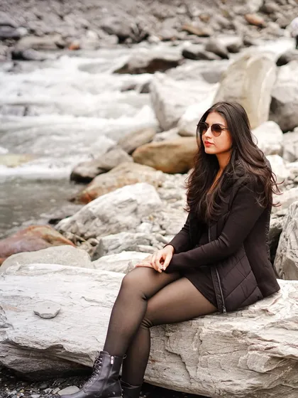 A beautiful solo shot of the bride-to-be sitting by a rocky stream in Manali, looking chic and thoughtful.