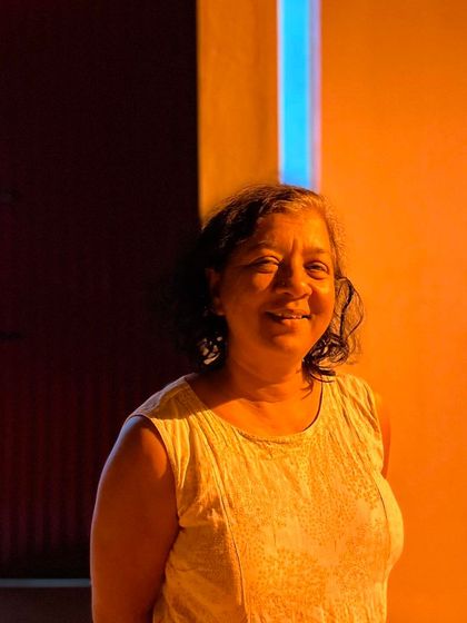 The artist Archana Hande, bathed in the warm glow of the evening light against a brightly colored wall in her home. The architecture here serves as a backdrop for the life and personality of its inhabitant.