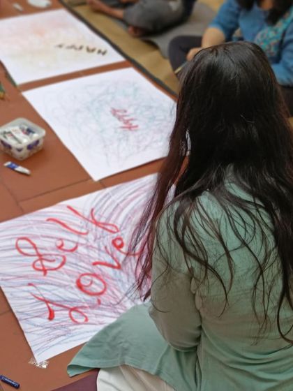 A participant lost in the process of creating a 'Self Love' art piece. These sessions are all about connecting with your inner self on the floor, with paper and colors.