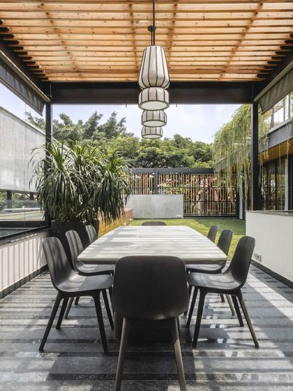 This outdoor covered dining deck is an inviting extension of the home, perfect for enjoying Bangalore's pleasant weather year-round. A wooden pergola provides partial shade.