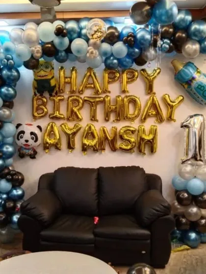 A first birthday party with a panda and Minion theme. This home setup features a blue, black, and silver balloon arch around a sofa, with character foil balloons and a number '1'.