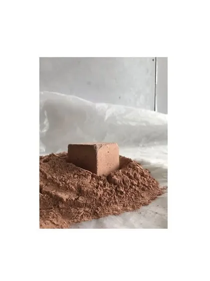 A block of earth-based plaster sits atop the raw material from which it was made. This simple image illustrates the transformative process of turning raw, local soil into a beautiful and durable building material.