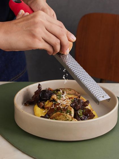 The finishing touch: grating smoked bandel cheese over the Chargrilled Exotic Mushrooms, adding a final layer of smoky, salty flavor.