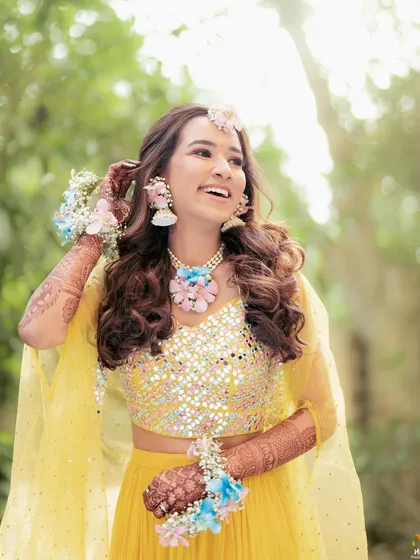 A happy and candid moment from the Haldi celebration. The bride's pastel floral jewellery adds a touch of softness to her bright and cheerful look.