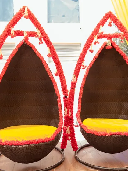 Unique swing chairs decorated with red floral garlands, providing stylish and fun seating for the Haldi ceremony.
