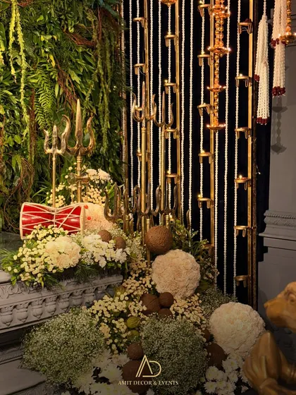 A beautiful composition of traditional elements at the altar, including brass trishuls, a damru drum, and coconuts, all nestled in a bed of white flowers.