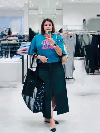 A mirror selfie in a store, wearing a graphic tee, a long denim skirt, and carrying a large tote bag. A perfect example of a casual shopping day outfit.