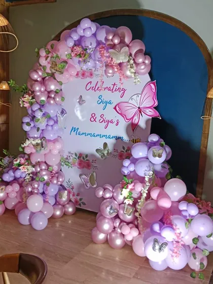 An elaborate butterfly-themed celebration with a custom arched backdrop and a lush balloon garland in shades of pink and purple.