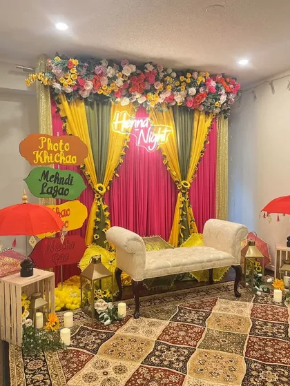 We love adding fun, personal touches to your Mehndi night. This cozy setup features a custom neon sign and a quirky "Photo Khichao, Mehndi Lagao" signboard, creating a perfect, Instagrammable corner for guests to enjoy.