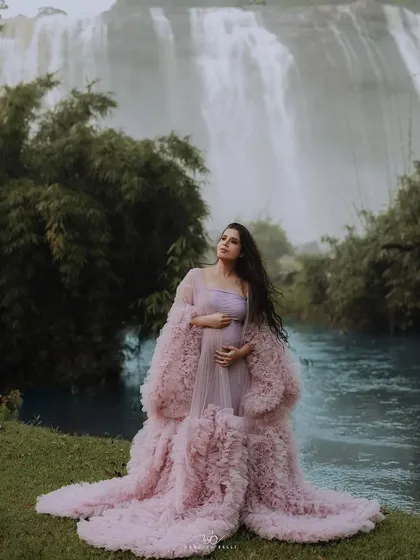 A serene monsoon maternity shoot. This client looks absolutely peaceful in a light pink ruffled gown with a matching sheer robe, set against a stunning waterfall. The soft fabric and design are perfect for capturing tranquil moments.