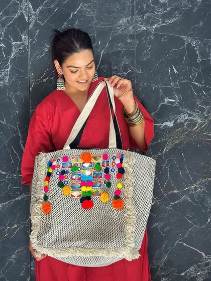 I love playing with color, and this tote bag is all about celebrating vibrant Indian crafts. The combination of intricate mirror work and playful, multi-colored pom-poms makes it a joyful statement piece that adds instant energy to a simple ethnic outfit.