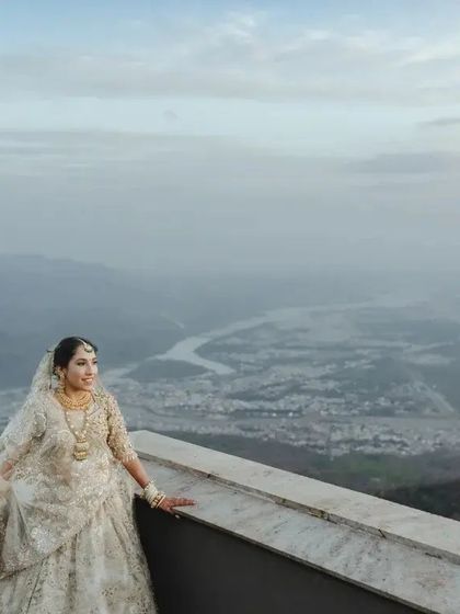 A breathtaking wide shot of the bride on a balcony overlooking a river winding through the mountains. This portrait is all about scale, showing the bride as a regal figure in a vast, beautiful landscape.