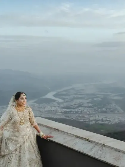 A breathtaking wide-angle shot of the bride on a terrace, with a vast river and valley below, showcasing the epic scale of the location.