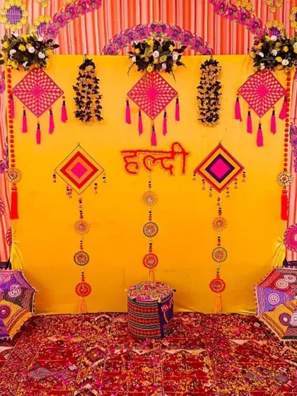 This is a classic Haldi ceremony backdrop I created, filled with traditional elements. The vibrant yellow cloth is decorated with colorful tassels and Rajasthani-style umbrellas, creating a festive and picture-perfect setting for your home function.