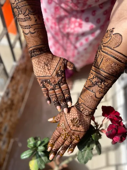 This back-of-hand design features a lotus on one palm and a peacock on the other, with personalized initials. The photo, taken in natural light with a flower, highlights the beauty of the design.