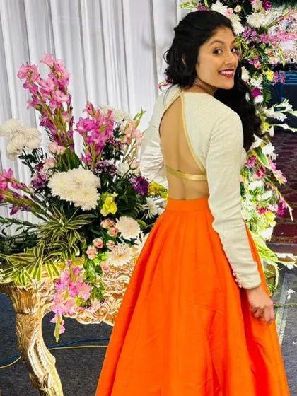 A fun and vibrant lehenga with a bright orange skirt and a white, full-sleeved crop top with a daring open back.