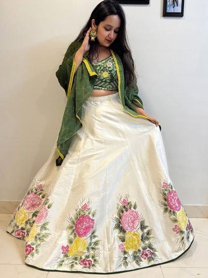This stunning lehenga features a unique combination of an off-white, hand-painted floral skirt and a richly embroidered green blouse. It's an artistic and elegant choice for a mehendi or sangeet.