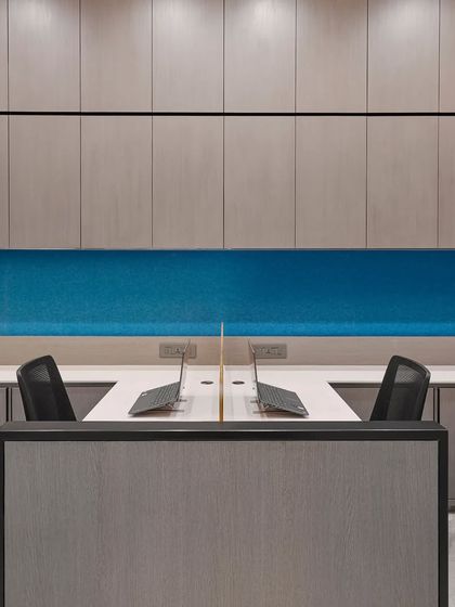 A clean and organized workstation setup with a calming blue backdrop. The design prioritizes functionality with built-in overhead storage and an uncluttered desk surface.