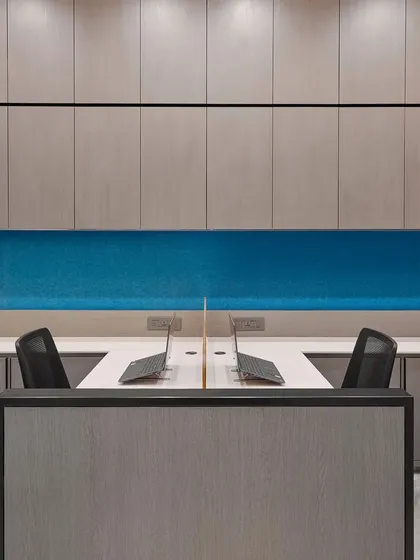 A clean and organized workstation setup with a calming blue backdrop. The design prioritizes functionality with built-in overhead storage and an uncluttered desk surface.