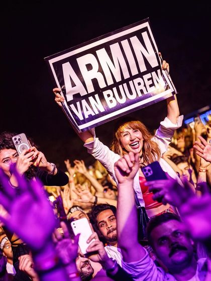 Pure joy on a fan's face as she holds up a sign for Armin Van Buuren, surrounded by a crowd of fellow trance lovers.
