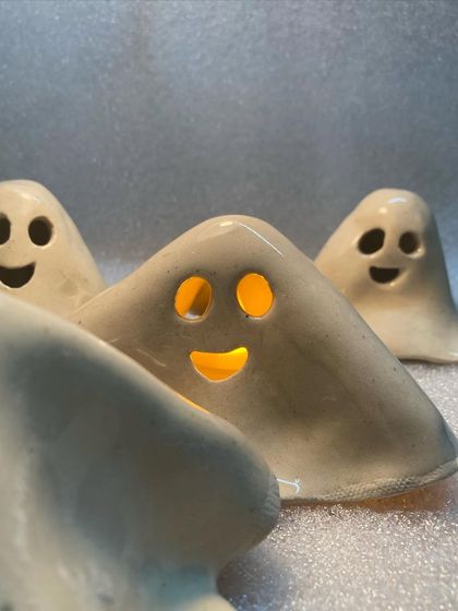 A group of my ghost tea light holders, glowing warmly. They are perfect for Halloween, but their cheerful faces make them a fun decoration for any time of year.